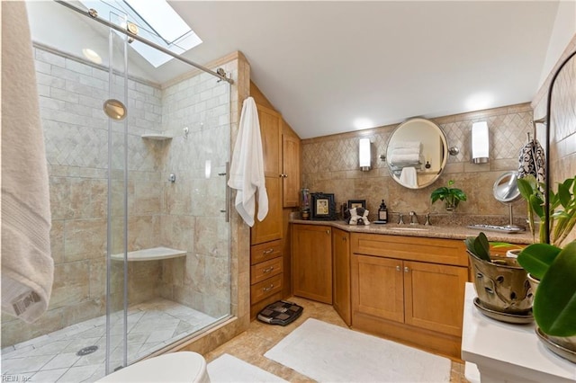 bathroom with a stall shower, vaulted ceiling with skylight, tasteful backsplash, vanity, and tile walls