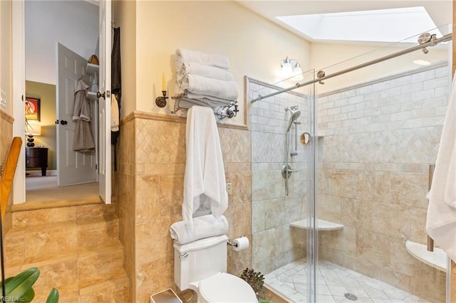 full bathroom featuring a wainscoted wall, a shower stall, toilet, and tile walls