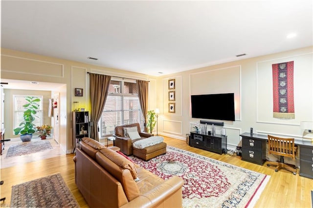 living room with light wood-style floors, visible vents, and a decorative wall