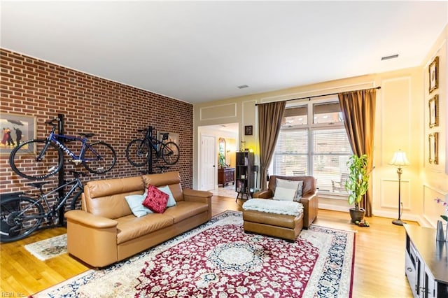 living room with visible vents, brick wall, and wood finished floors