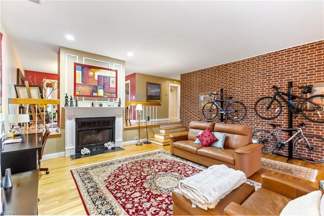 living room with baseboards, brick wall, wood finished floors, a fireplace, and recessed lighting