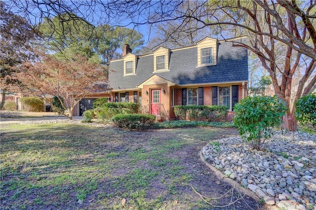 colonial inspired home with a shingled roof, a front yard, brick siding, and a chimney