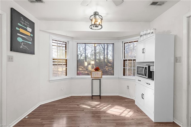 unfurnished dining area with a healthy amount of sunlight, visible vents, baseboards, and wood finished floors