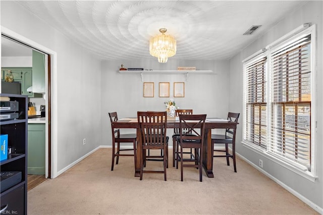 carpeted dining room with visible vents, baseboards, and an inviting chandelier