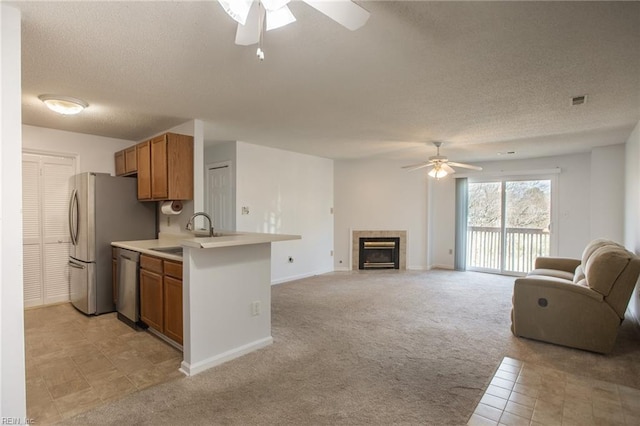 kitchen with light carpet, brown cabinetry, open floor plan, a sink, and stainless steel dishwasher