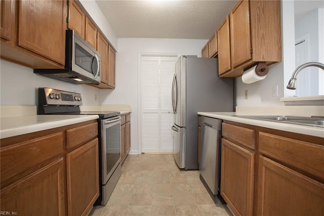 kitchen featuring brown cabinets, appliances with stainless steel finishes, light countertops, and a sink