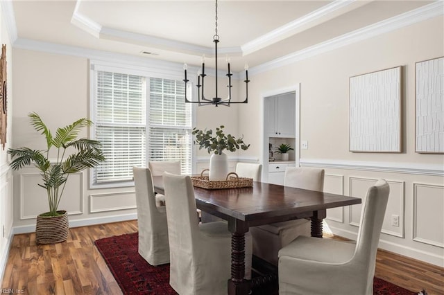 dining area featuring crown molding, a raised ceiling, a decorative wall, and wood finished floors