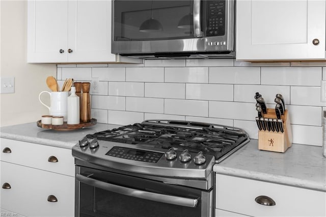 kitchen featuring stainless steel appliances, light stone countertops, white cabinetry, and decorative backsplash