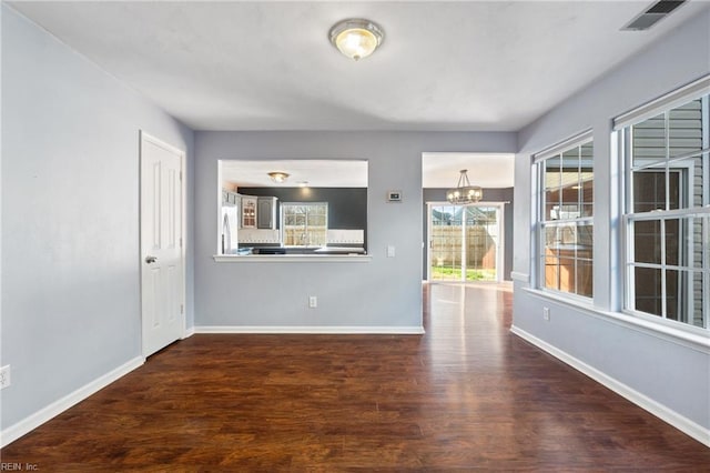 spare room featuring a notable chandelier, dark wood-style flooring, visible vents, and baseboards