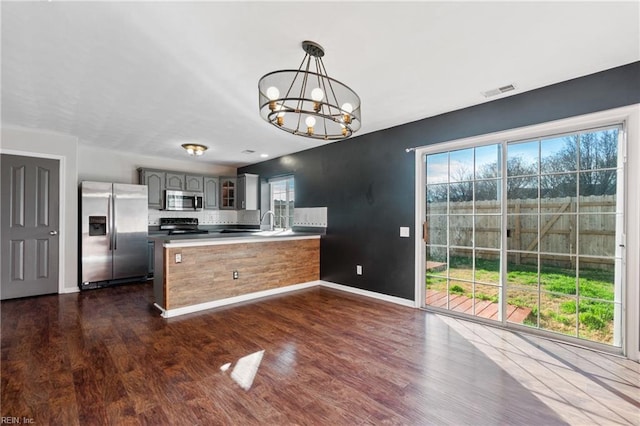 kitchen featuring a notable chandelier, stainless steel appliances, baseboards, gray cabinets, and dark wood-style floors