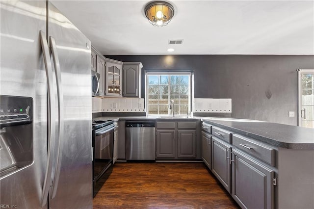 kitchen with stainless steel appliances, a sink, visible vents, gray cabinets, and dark countertops