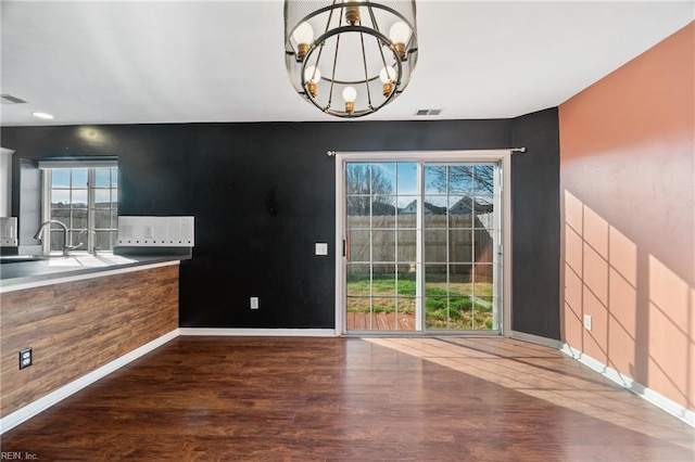 unfurnished dining area featuring baseboards, visible vents, dark wood-style floors, a notable chandelier, and a sink