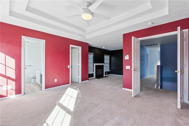 spare room featuring visible vents, light colored carpet, ceiling fan, a fireplace with flush hearth, and a tray ceiling