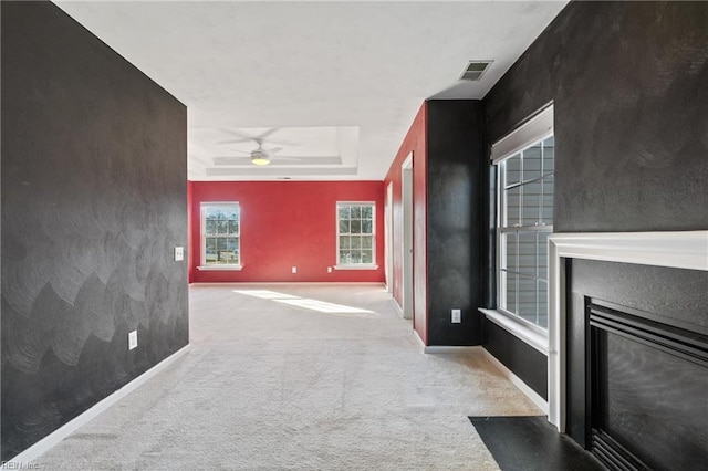 living room featuring light colored carpet, a fireplace with flush hearth, visible vents, baseboards, and a tray ceiling