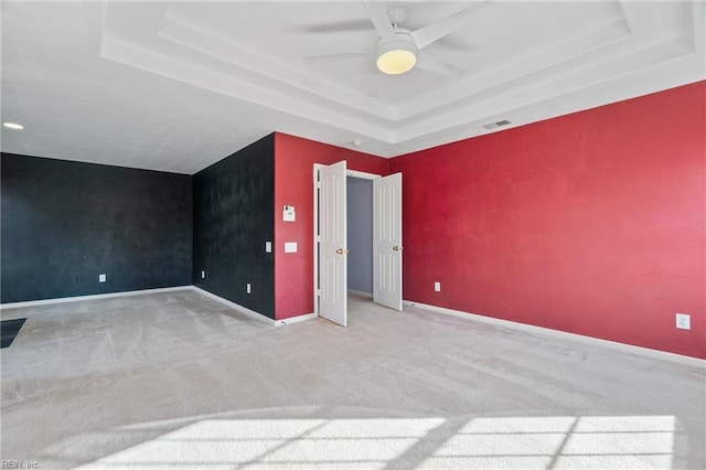 unfurnished bedroom with an accent wall, a tray ceiling, light colored carpet, and baseboards