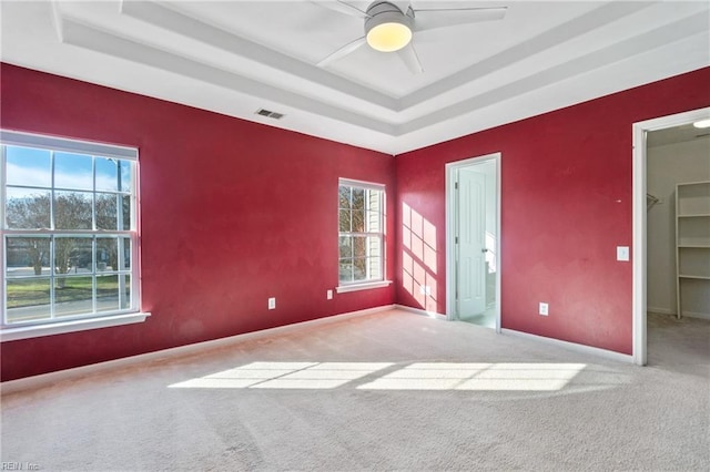 carpeted empty room featuring baseboards, visible vents, a raised ceiling, and a ceiling fan