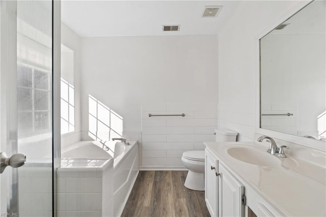 bathroom featuring toilet, a wainscoted wall, wood finished floors, vanity, and a bath