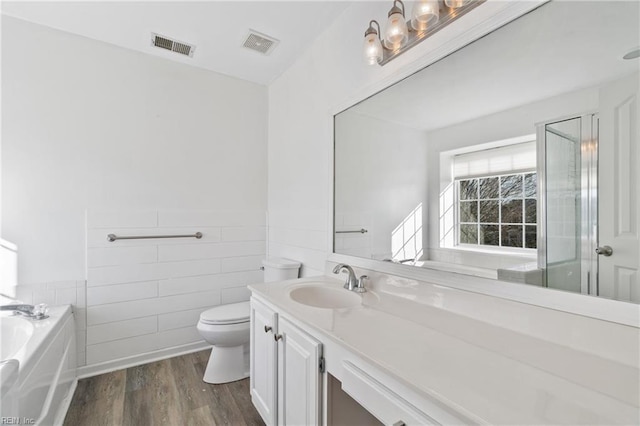 bathroom with a wainscoted wall, wood finished floors, vanity, visible vents, and tile walls