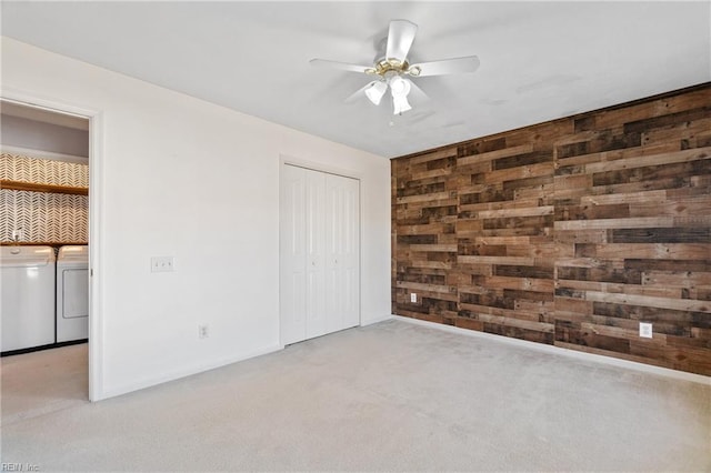 unfurnished bedroom featuring light carpet, an accent wall, wood walls, washer and dryer, and a closet