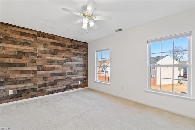 unfurnished room featuring wooden walls, an accent wall, carpet flooring, a ceiling fan, and visible vents