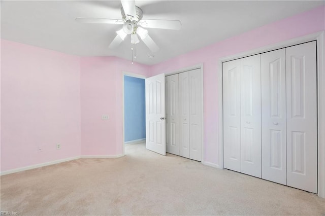 unfurnished bedroom featuring a ceiling fan, baseboards, two closets, and light colored carpet