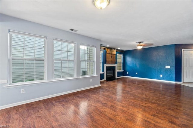 unfurnished living room featuring a glass covered fireplace, visible vents, baseboards, and wood finished floors