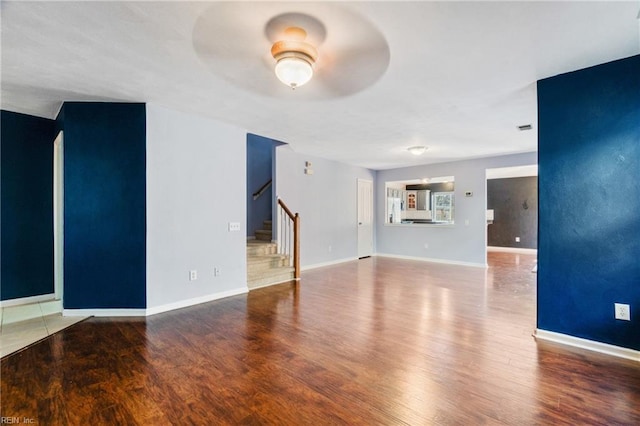 unfurnished living room with ceiling fan, stairway, baseboards, and wood finished floors