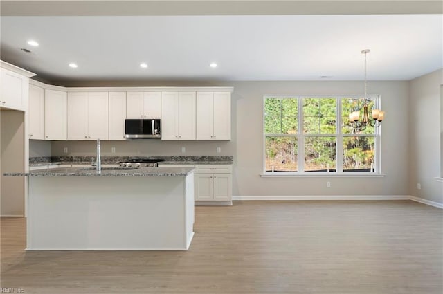 kitchen featuring light stone counters, recessed lighting, stainless steel microwave, and light wood finished floors