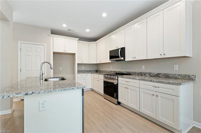 kitchen featuring light stone counters, recessed lighting, light wood-style flooring, appliances with stainless steel finishes, and a sink