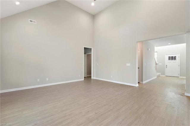 unfurnished room with high vaulted ceiling, visible vents, light wood-style flooring, and baseboards