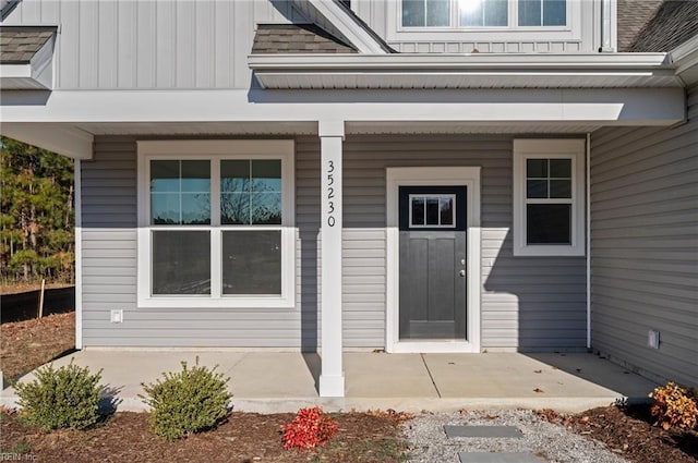 property entrance featuring covered porch, a shingled roof, and board and batten siding