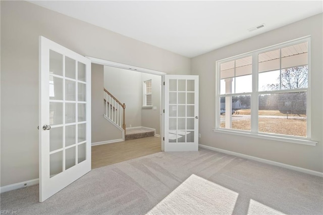 carpeted empty room featuring visible vents, stairway, baseboards, and french doors