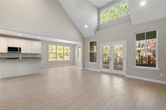 unfurnished living room featuring high vaulted ceiling, french doors, light wood-type flooring, and baseboards