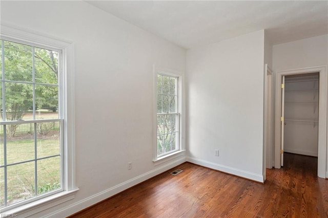 unfurnished bedroom featuring visible vents, multiple windows, baseboards, and wood finished floors