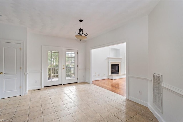 interior space featuring light tile patterned floors, a glass covered fireplace, visible vents, and baseboards