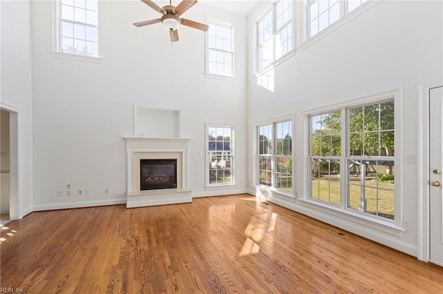 unfurnished living room with wood finished floors, plenty of natural light, a glass covered fireplace, and baseboards