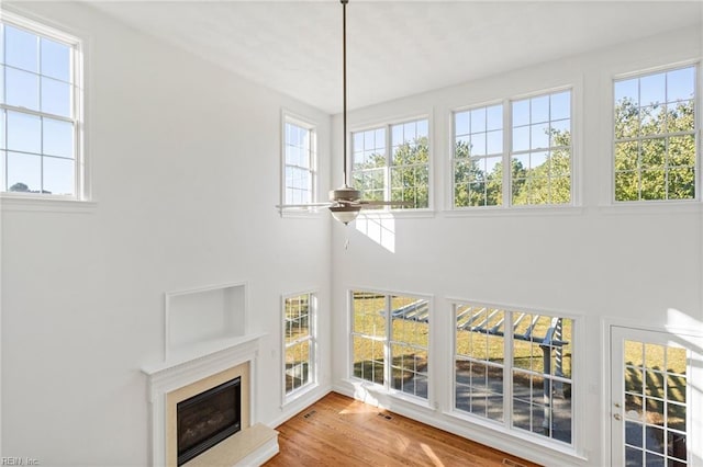 unfurnished living room with visible vents, a towering ceiling, ceiling fan, a premium fireplace, and wood finished floors