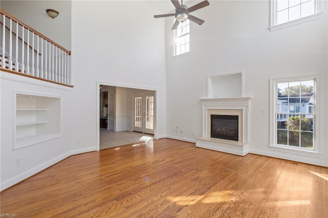 unfurnished living room featuring built in shelves, wood finished floors, a glass covered fireplace, and baseboards