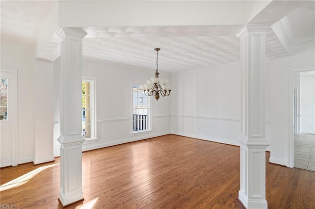 unfurnished dining area featuring crown molding, a notable chandelier, decorative columns, wood finished floors, and baseboards