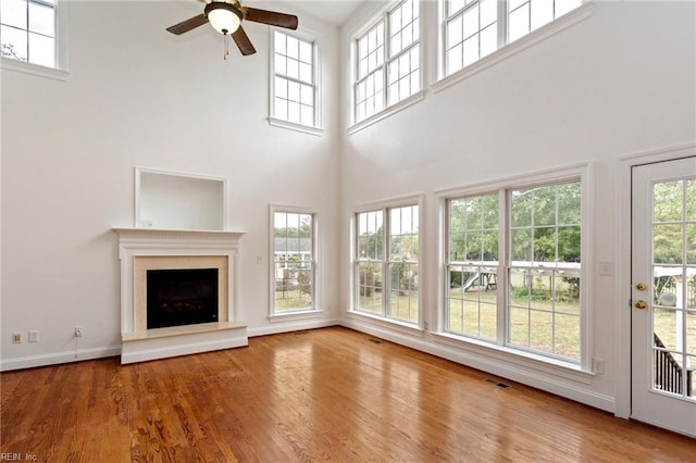 unfurnished living room with baseboards, visible vents, a fireplace with raised hearth, ceiling fan, and wood finished floors