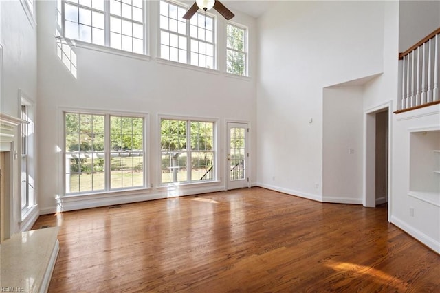 unfurnished living room featuring a high ceiling, wood finished floors, a ceiling fan, a high end fireplace, and baseboards