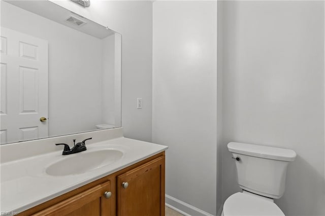 bathroom with toilet, vanity, visible vents, and baseboards