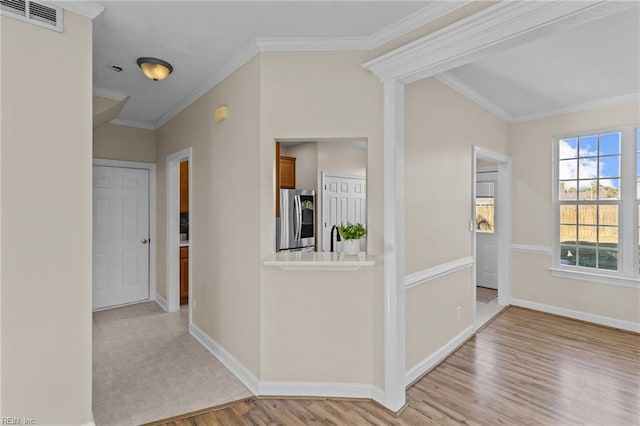 corridor featuring light wood finished floors, ornamental molding, visible vents, and baseboards