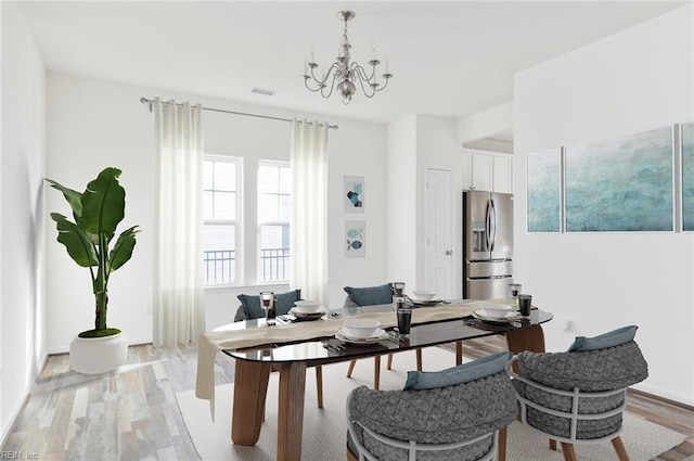 dining area with visible vents, light wood-style flooring, and an inviting chandelier