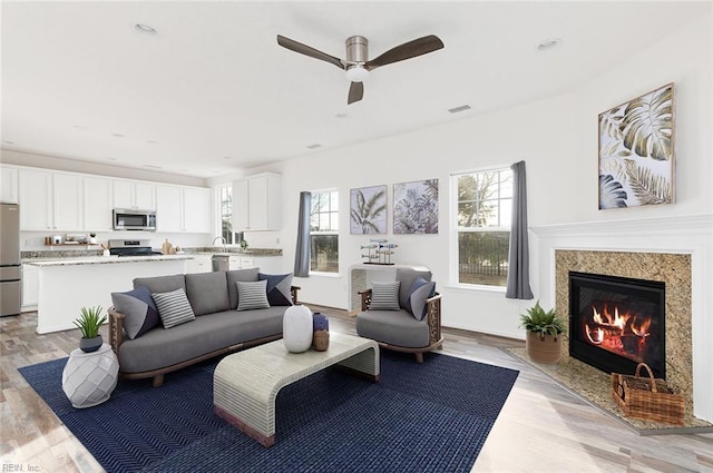 living area with recessed lighting, visible vents, light wood-style flooring, a premium fireplace, and a ceiling fan