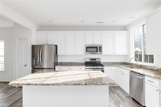 kitchen featuring a kitchen island, white cabinetry, stainless steel appliances, and a sink