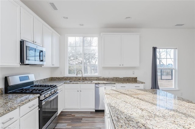 kitchen with white cabinets, appliances with stainless steel finishes, light stone countertops, light wood-type flooring, and a sink