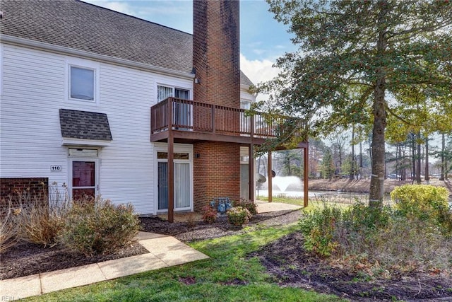 back of house with a shingled roof, a chimney, and a balcony