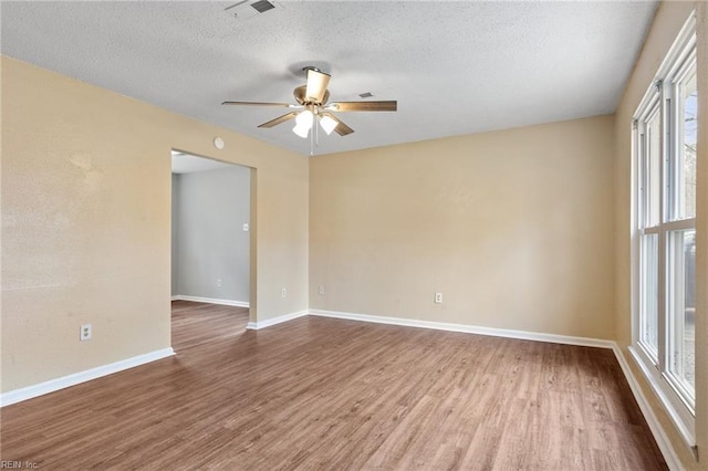 empty room with visible vents, a ceiling fan, a textured ceiling, wood finished floors, and baseboards