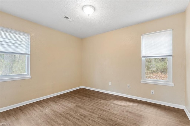 empty room with baseboards, plenty of natural light, visible vents, and wood finished floors